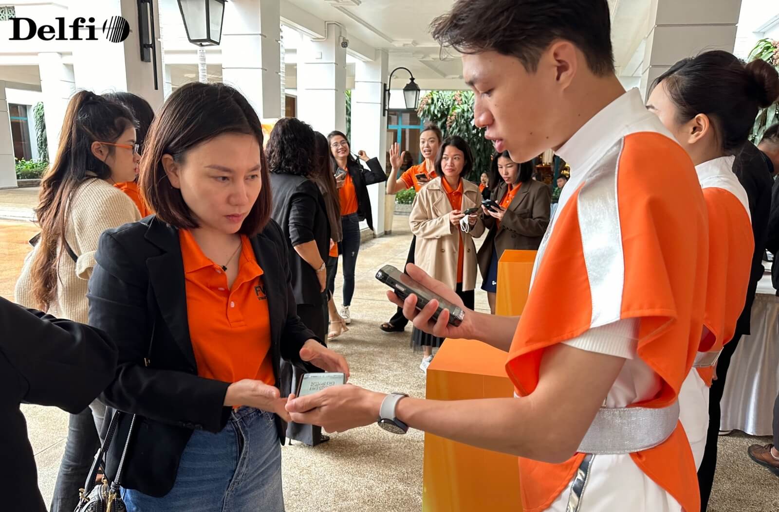 Nhân viên sự kiện đang hỗ trợ khách tham dự quét mã check-in bằng điện thoại tại khu vực tiếp đón.